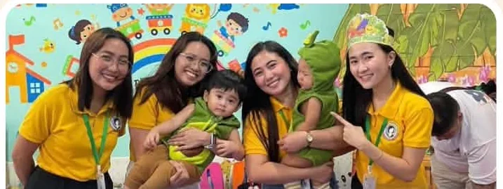Four Teacher A's teachers in yellow uniforms smiling with a toddler